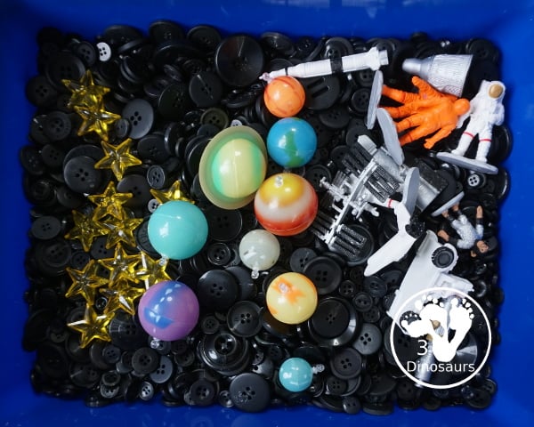 Space Button Sensory Bin - a simple sensory bin for a space theme with planets, space figures and stars in a black button filler for the sensory bin. 3Dinosaurs.com