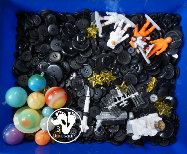 Space Button Sensory Bin - a simple sensory bin for a space theme with planets, space figures and stars in a black button filler for the sensory bin. 3Dinosaurs.com