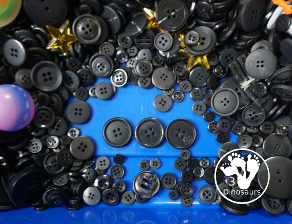 Space Button Sensory Bin - a simple sensory bin for a space theme with planets, space figures and stars in a black button filler for the sensory bin. 3Dinosaurs.com