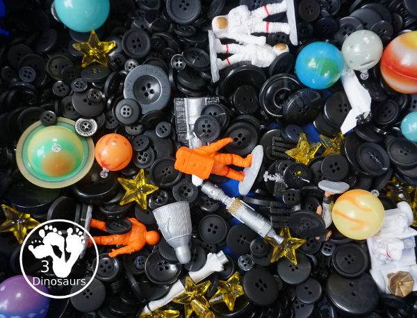 Space Button Sensory Bin - a simple sensory bin for a space theme with planets, space figures and stars in a black button filler for the sensory bin. 3Dinosaurs.com